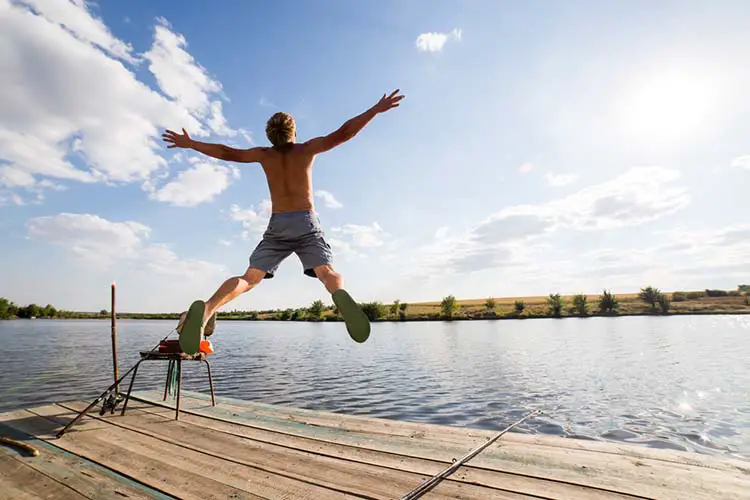 Happy man jumping on pier with lake and sky in background