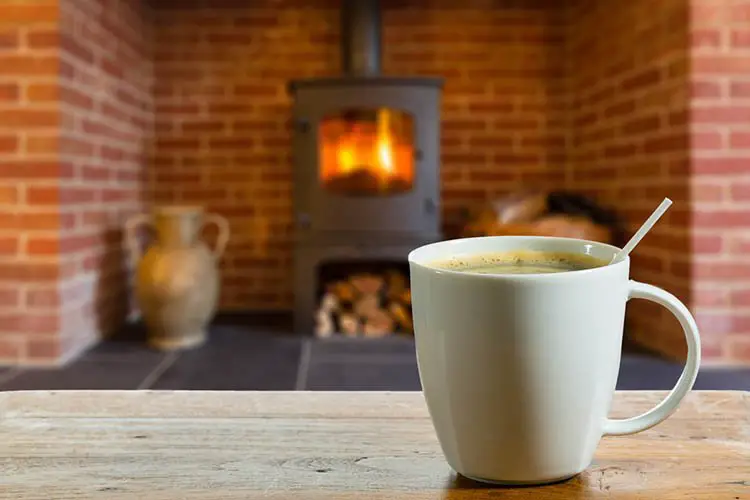 Coffee cup on wooden table in front of roaring fire