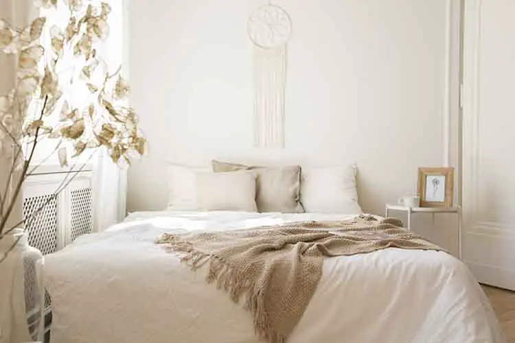 Blanket on white bed with cushions in minimal bedroom interior