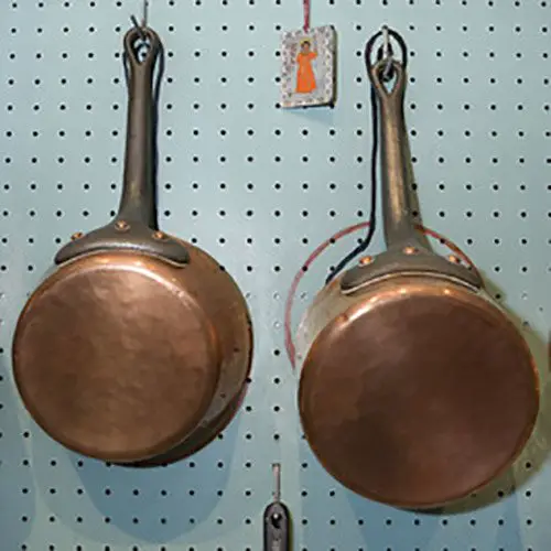 Two of the copper pots hanging on Julia Child’s original blue-painted pegboard, showing the outlines for each pot.