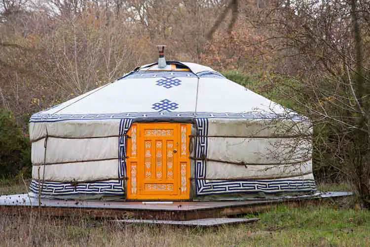 Close-up photo of one white yurt with blue simbols and big closed well-decorated orange door