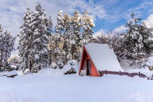 Small wooden mountain a-frame hut in winter, covered with snow