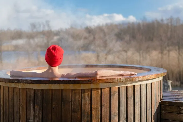 Young adult relaxing in wooden hot tub